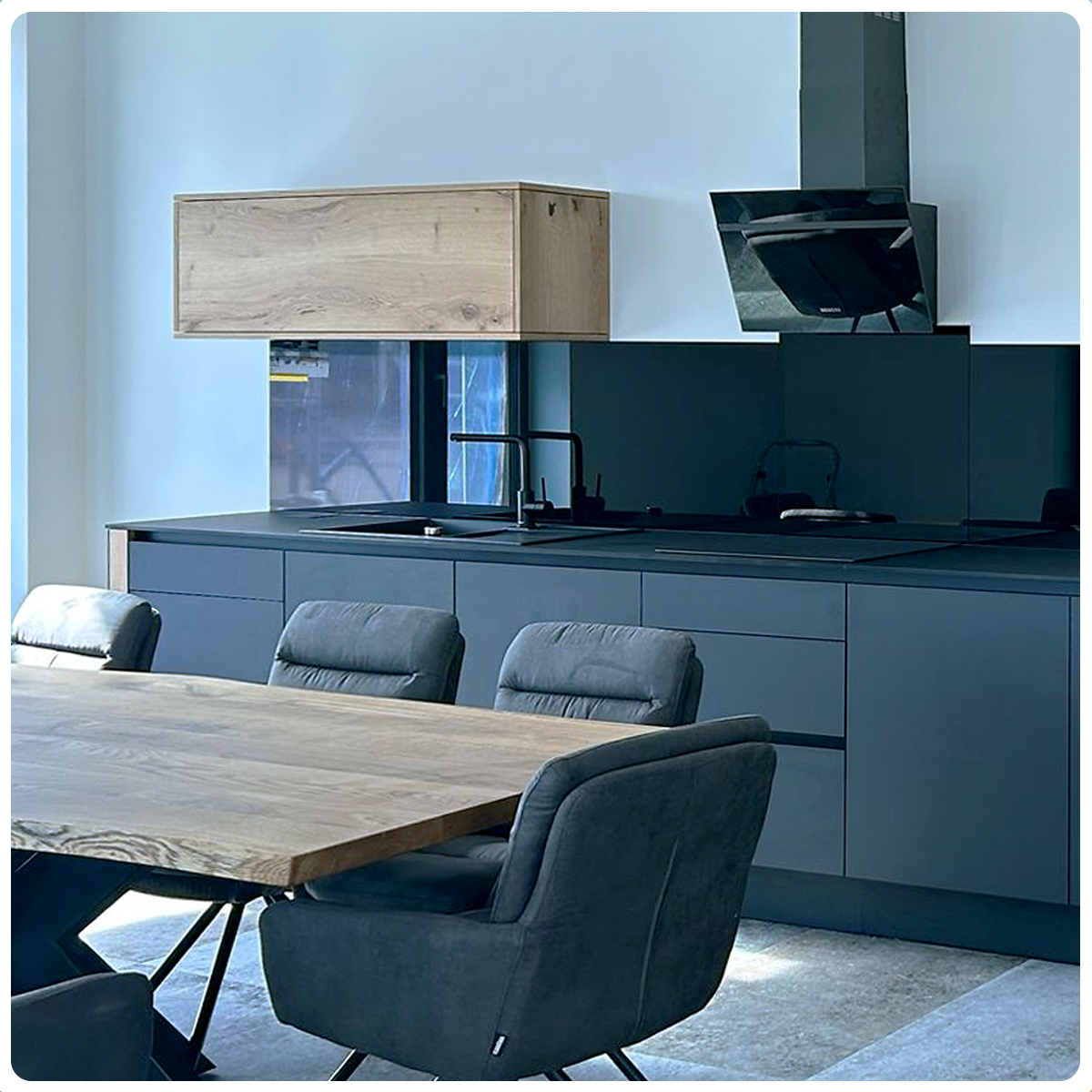 Massiver Tisch mit grauen Stühlen und im Hintergrund eine dunkel graue Küche.